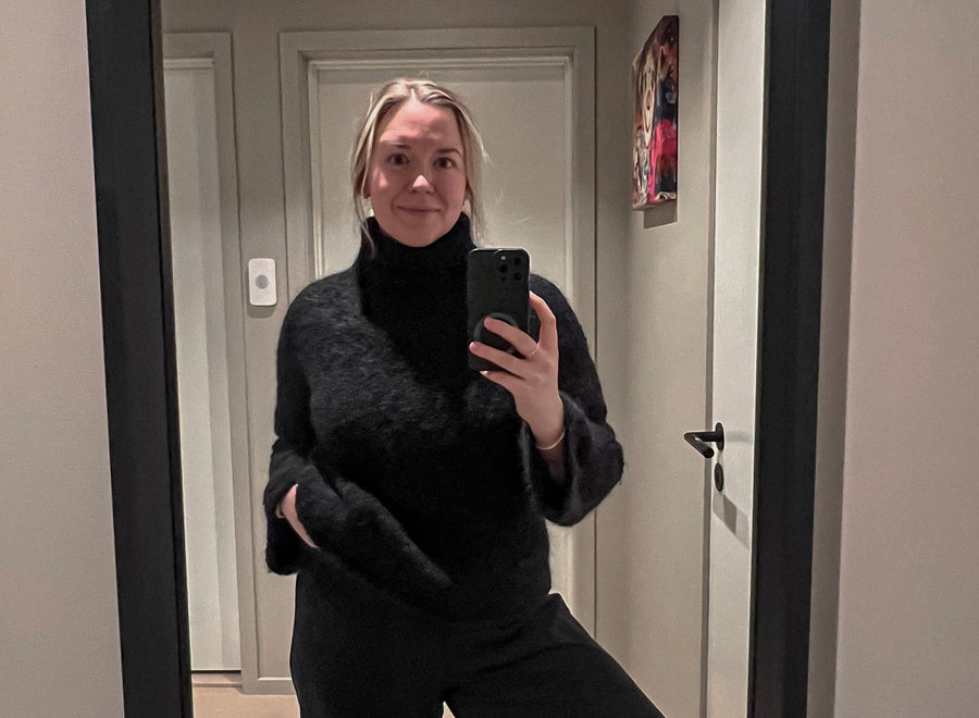 Kvinne som tar selfie i et speil i en svart strikkegenser og løse svarte bukser · genseren har en ren og rolig linje