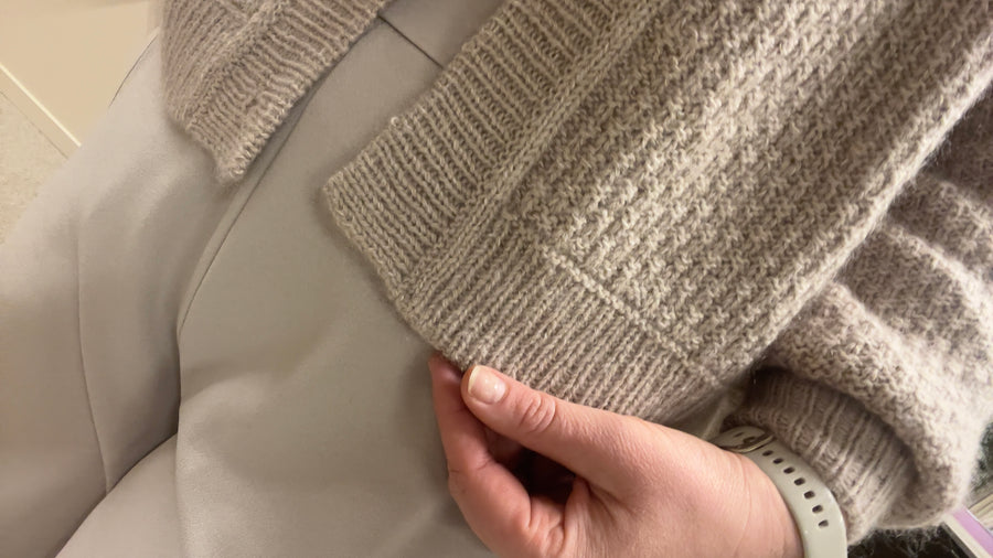 En hånd holder nederkanten, med vrangbord og struktur · samme størrelser som Mistlight Sweater