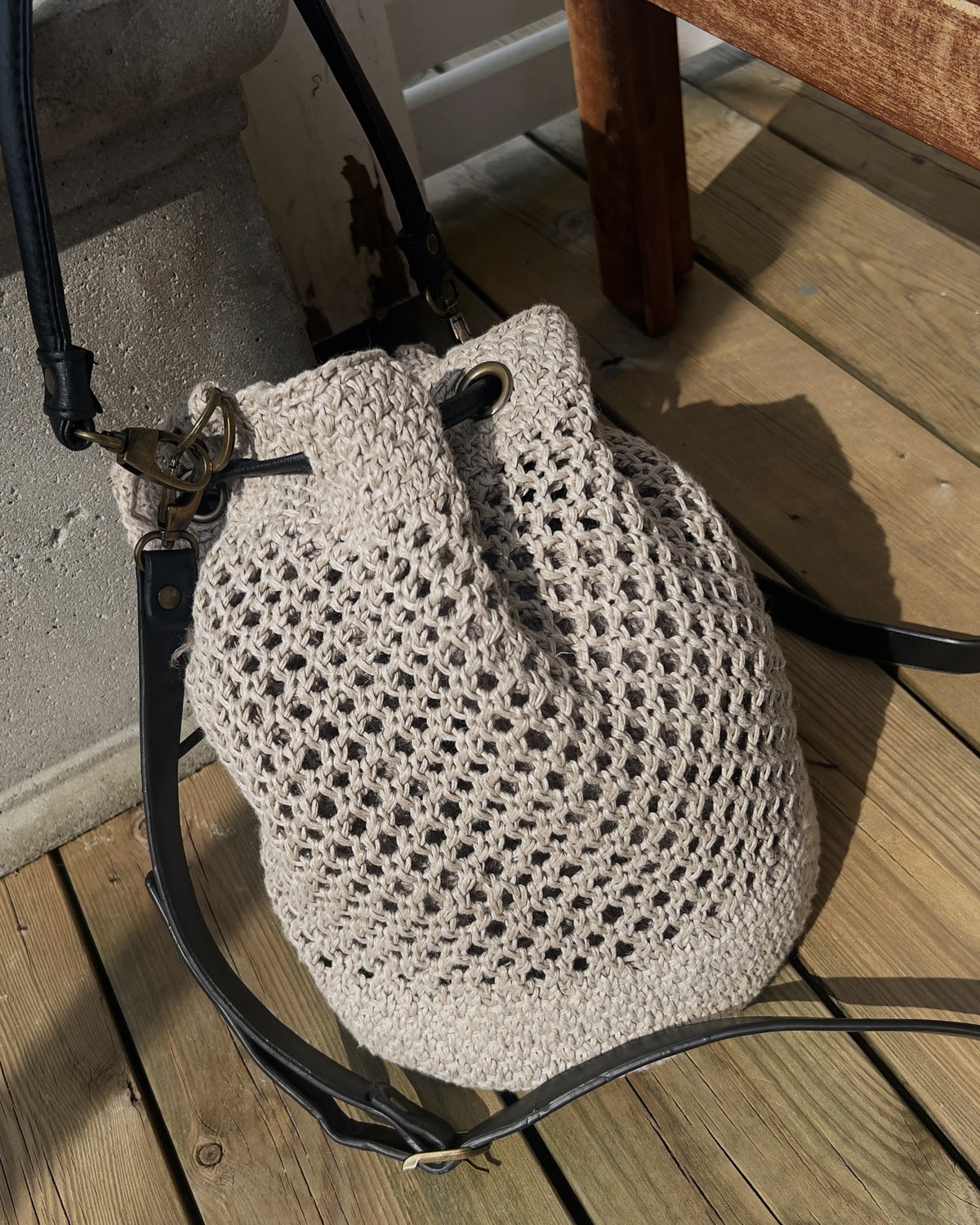 Bøttebag med langt skulderbånd på en treterrasse · nettmønster i midtpartiet