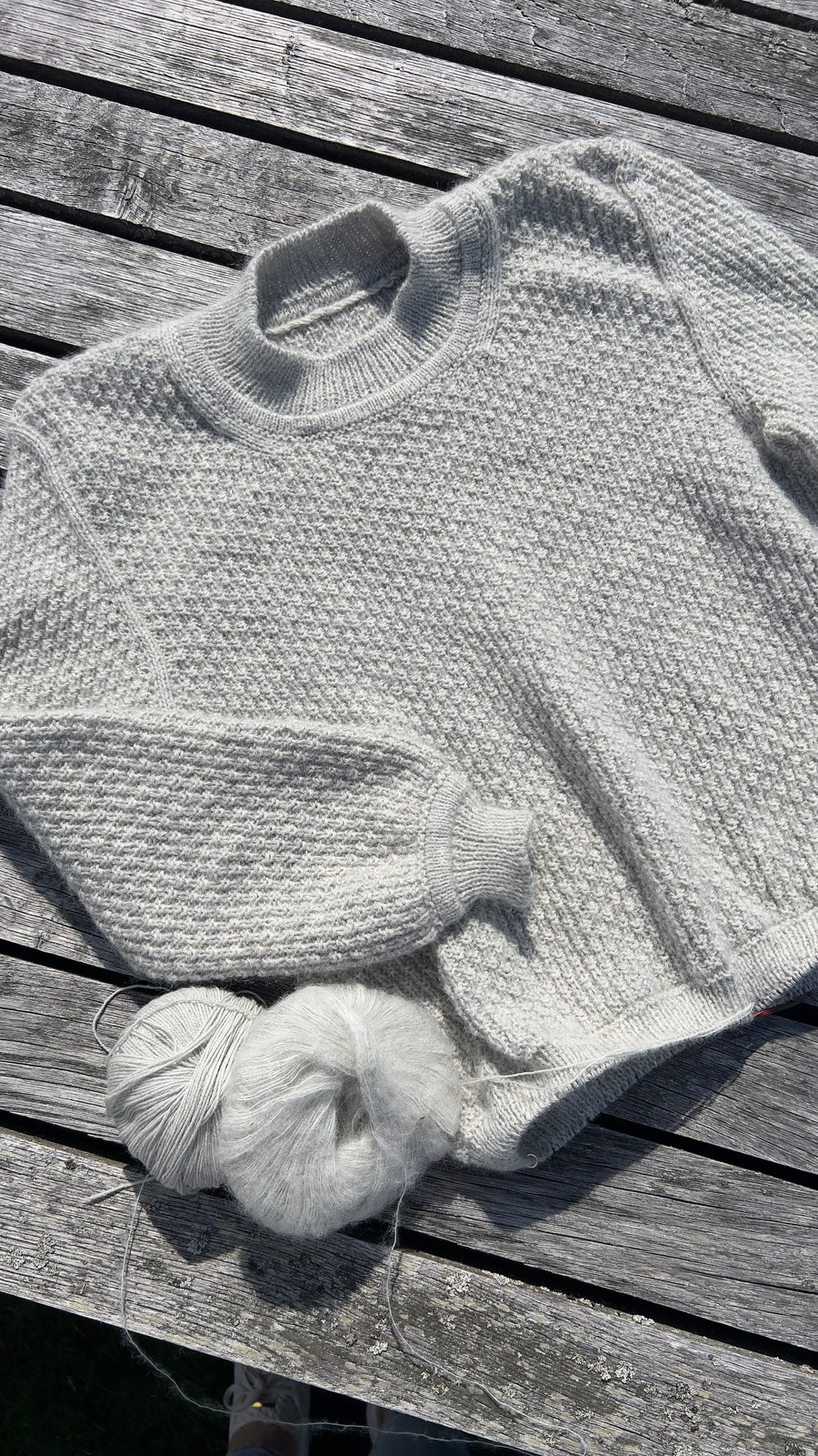 Mistlight Sweater liggende på forvitrede planker ved siden af to nøgler · garnet er Merino og Cashmere Mohair