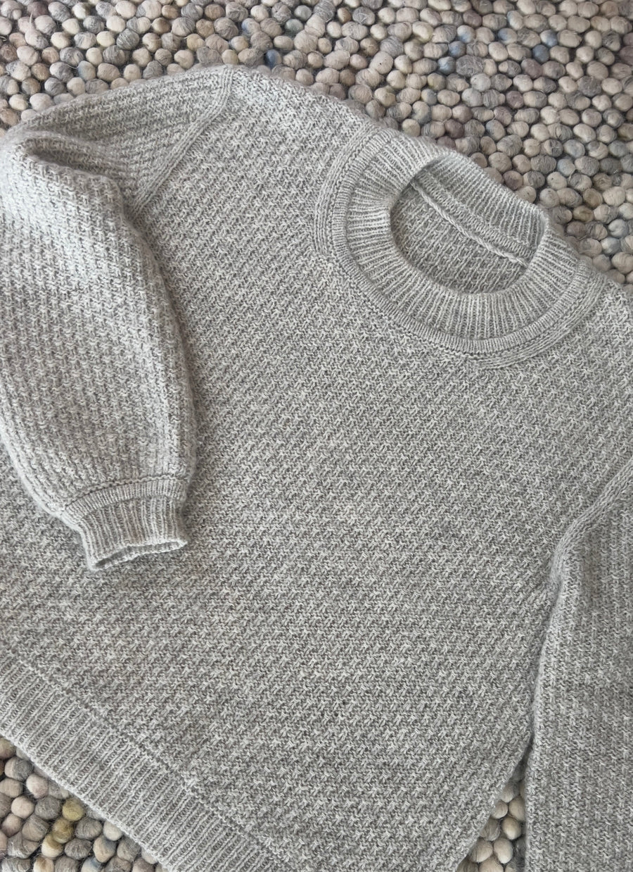 Mistlight Sweater liggende på et uldtæppe, med rund hals og ribbet manchet · strikkes oppefra og ned