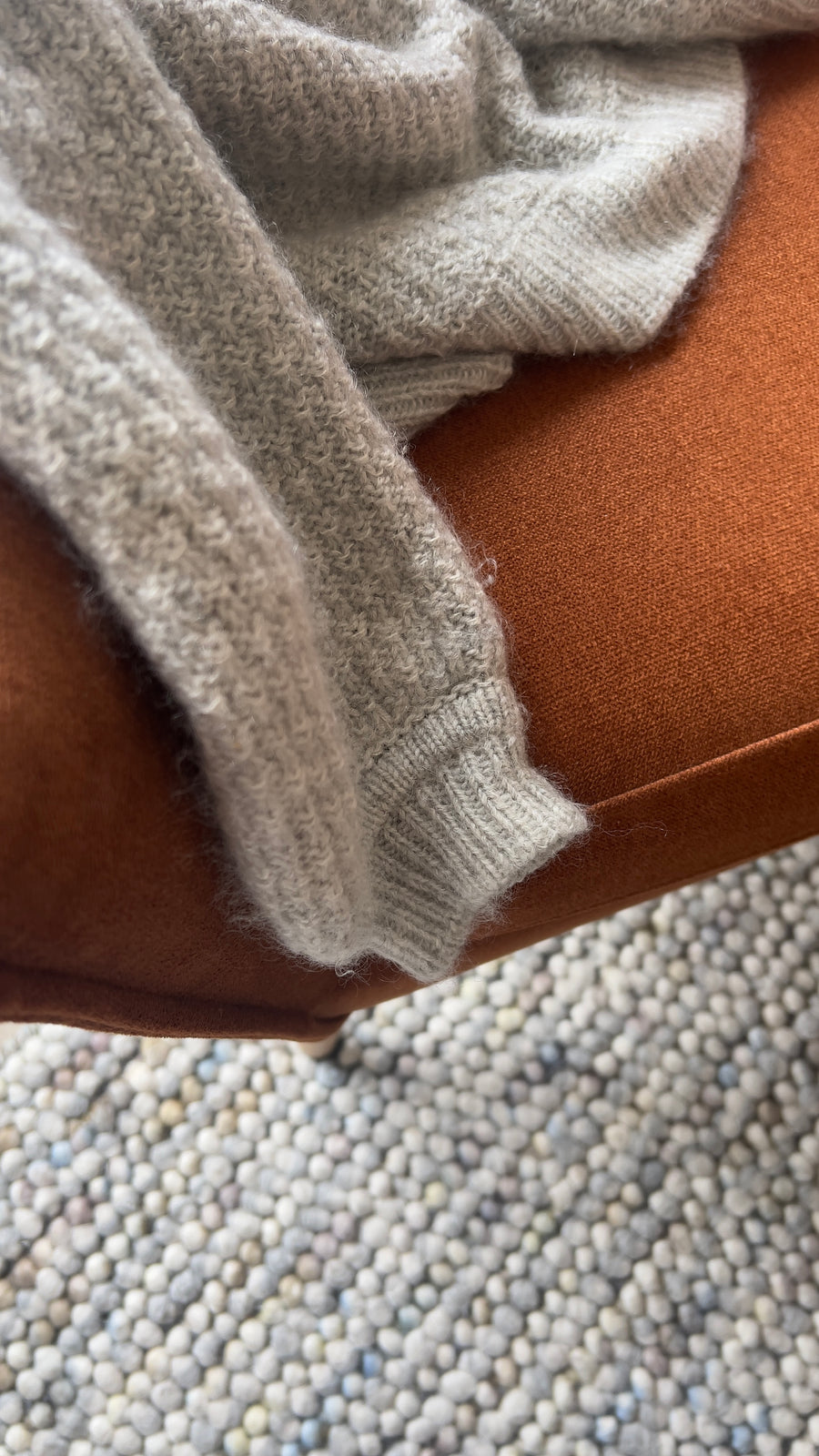 Ærme på Mistlight Sweater over en rustrød sofa, med ribbet manchet · samme størrelse kan sidde tættere eller løsere