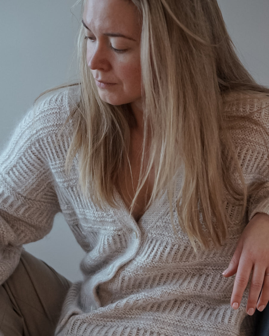Martine sitter med blikket ned, i en lys strikket cardigan med V-hals.