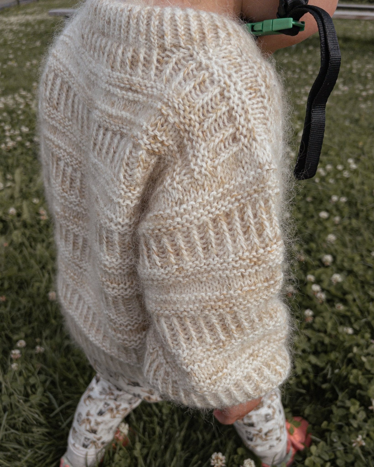 Ærme og side på Coffee Sweater Mini, i græsset · blødt garn holder barnet varmt