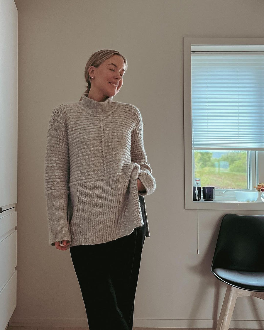 Dawn Sweater i fuld længde foran et vindue · den høje slids gør, at længden ikke føles tung