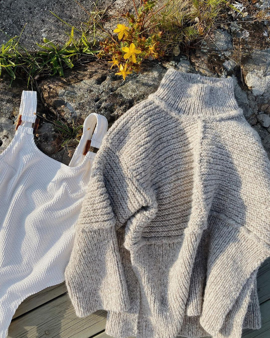 Dawn Sweater liggende på klippen ved gule blomster, ved siden af en hvid top · garnet er Alpaca 3