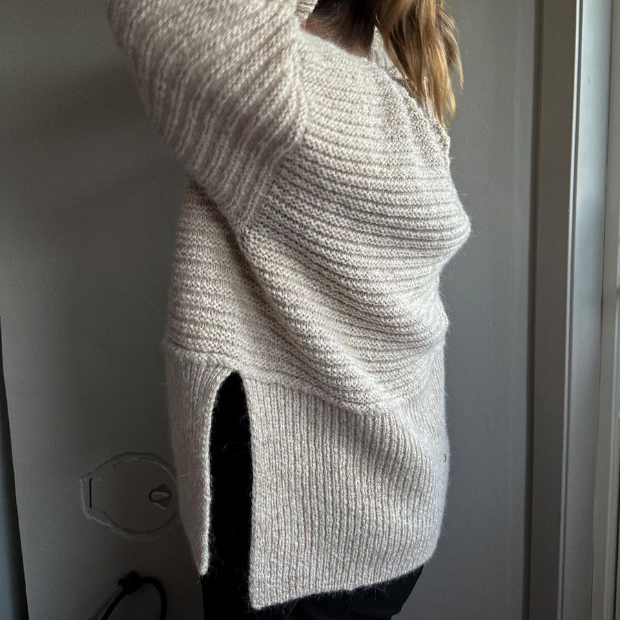 Cremefarvet Dawn Sweater set fra siden, med slids i den ribbede nederkant · kroppen strikkes i ét stykke