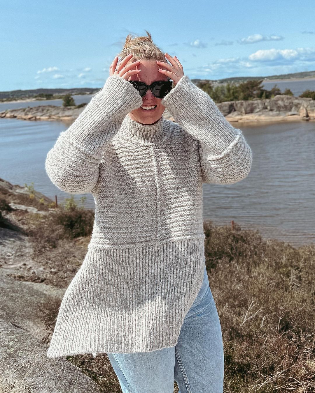 Dawn Sweater udendørs ved havet, med hænderne op mod ansigtet · strikkes oppefra og ned