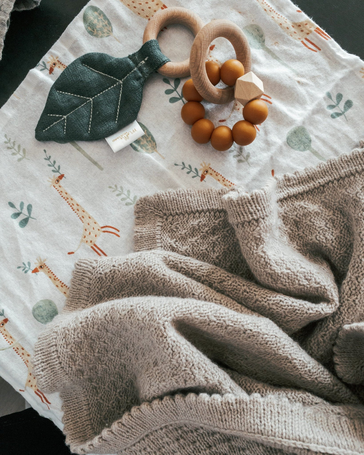 Granola-tæppe på et dug med girafmønster og legetøj i træ · samme struktur som Granola Sweater